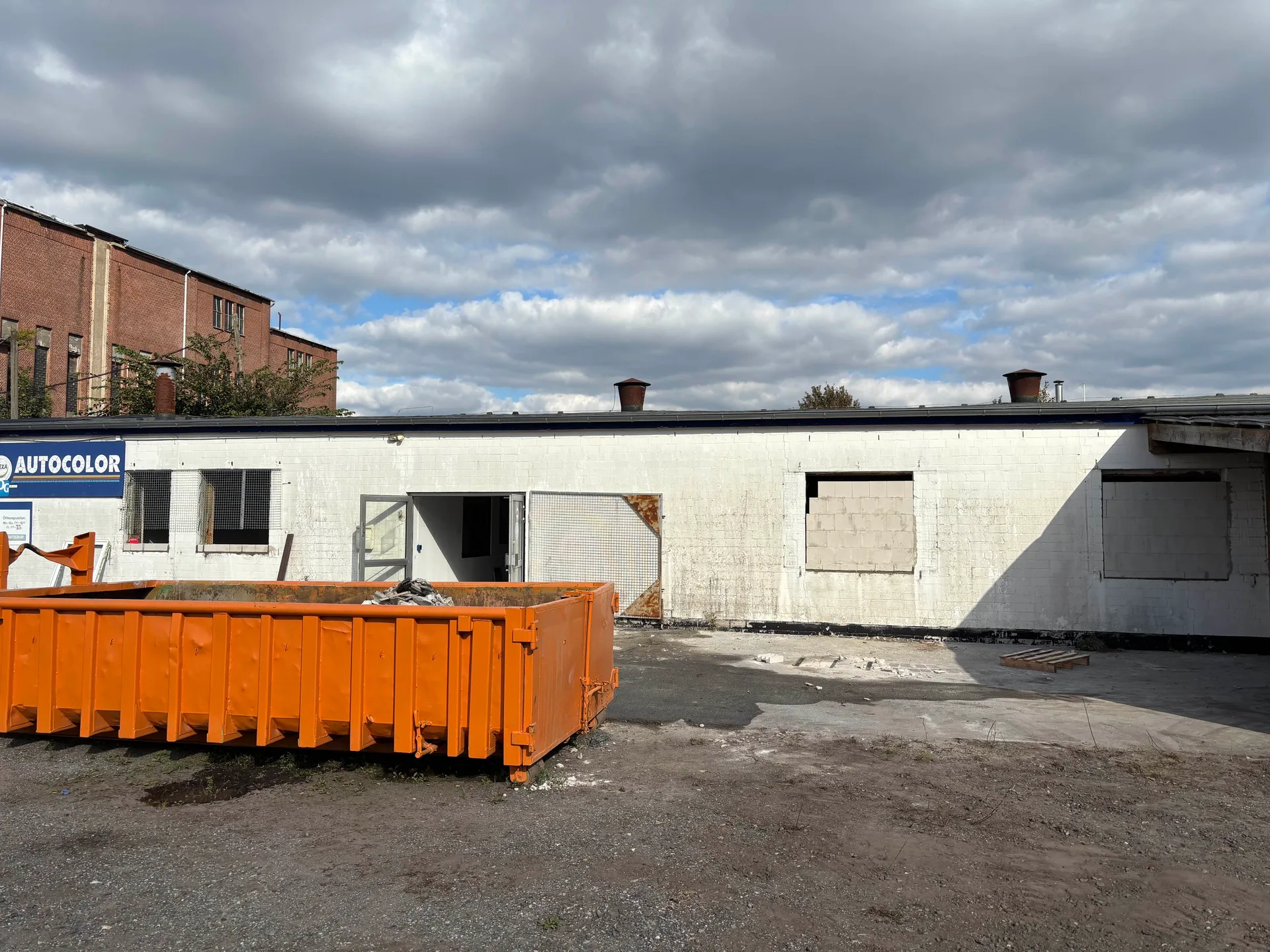Erste Abrissphase: Fensteröffnungen bereits gebrochen, Abrollcontainer vor dem Eingang